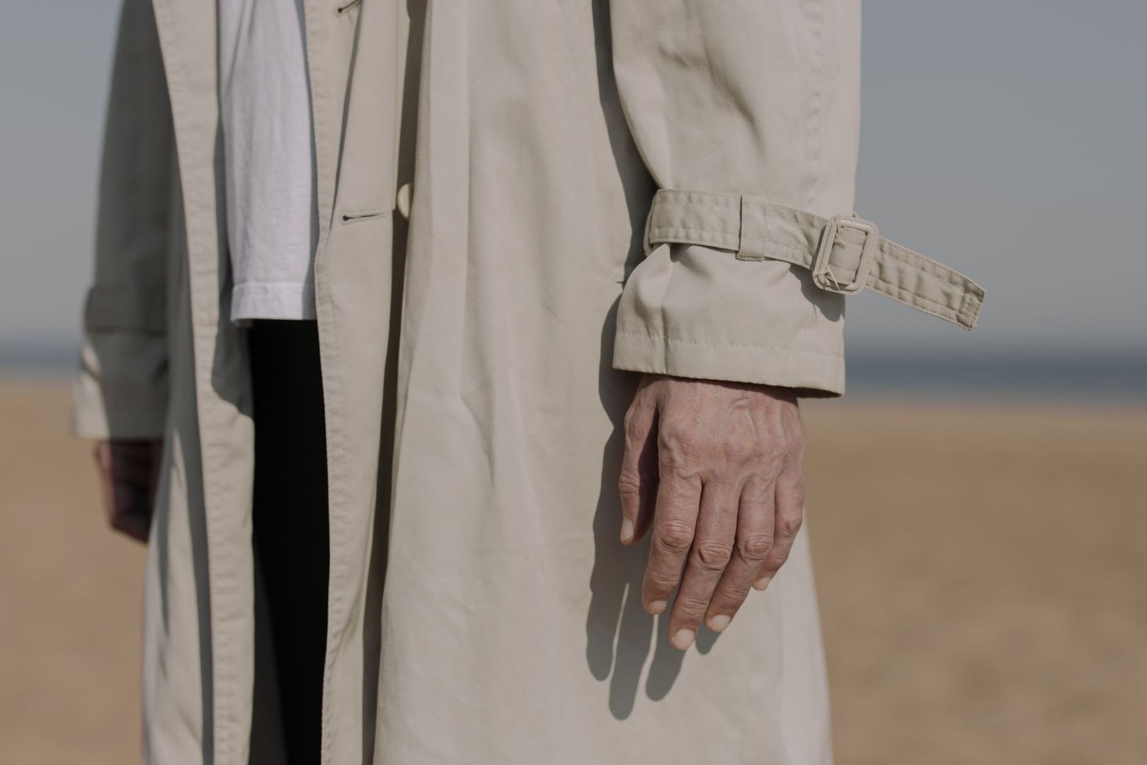 Närbild av en ljus trenchcoat med bälte och ärmslejf vid stranden